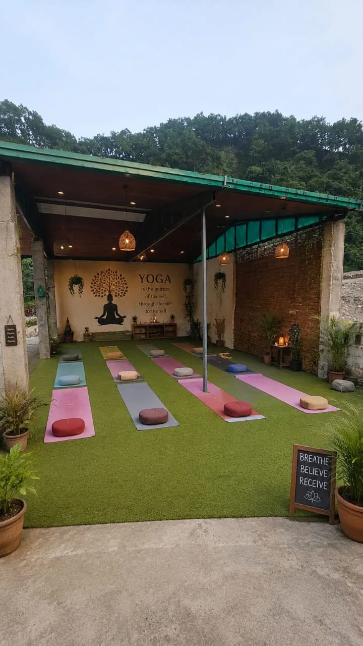 Open-air yoga hall with mats laid out, surrounded by greenery at the ashram in Rishikesh